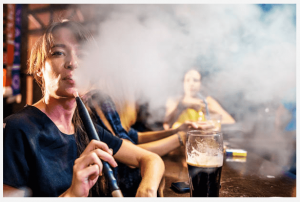 žena fajčí vodnú fajku v bare a vyfukuje hustý dym