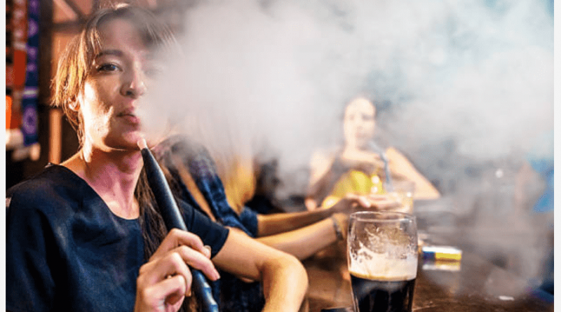 žena fajčí vodnú fajku v bare a vyfukuje hustý dym