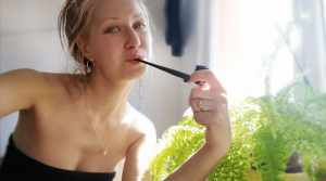 žena fajčí fajku na tabak pri okne a papradí