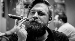 mladý muž má upravenú bradu a fajčí cigaru