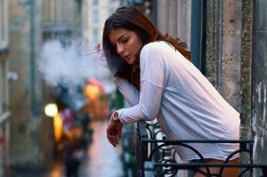 Žena fajčí na malom balkóne, pod ňou je rušná ulica