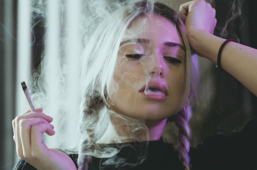 Mladá žena fajčí cigaretu, vydychuje dym