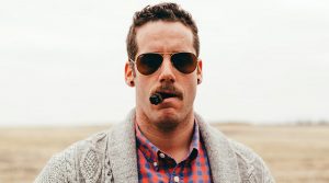 muž s cigarou v ústach má tunely v ušiach a letecké okuliare ray ban