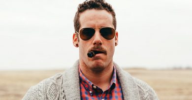 muž s cigarou v ústach má tunely v ušiach a letecké okuliare ray ban