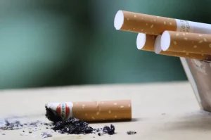 Cigaretové filtre v popolníku a jeden vypadnutý filter na stole obklopený cigaretovým popolom