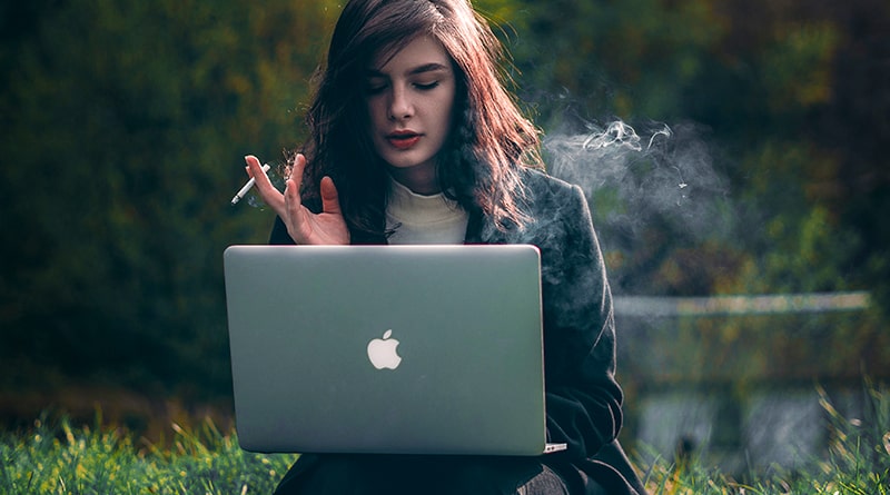 žena sedí v padku, na kolenách má notebook a fajčí cigaretu