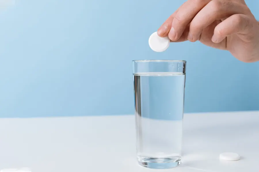 Ruka vhadzuje rozpustnú tabletu do pohára s vodou