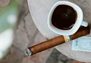 Horiaca cigara značky Cohiba položená na stole vedľa hrnčeku s čiernou kávou