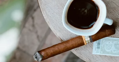 Horiaca cigara značky Cohiba položená na stole vedľa hrnčeku s čiernou kávou