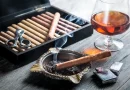 Cigary - príslušenstvo: humidor naplnený cigarami, kovový orezávač, horiaca cigara v kovovom popolníku, zapaľovač a pohár s likérom