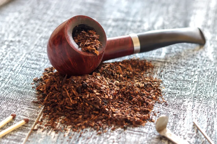 Briarová fajka na tabak položená na kôpke fajkového tabaku, fajkový príbor a zápalky na drevenom stole