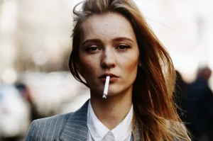 Mladá žena má v ústach zapálenú cigaretu - detailný záber hlavy a ramien