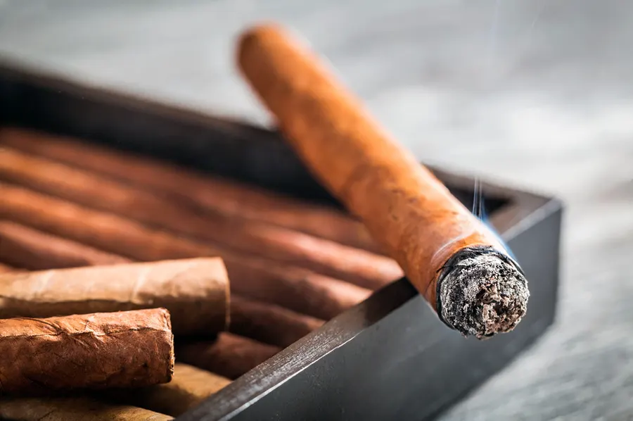 Horiaca cigara položená na okraji tmavého humidora s cigarami