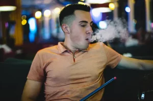 Detail: mladý muž fajčí vodnú fajku, vydychuje dym