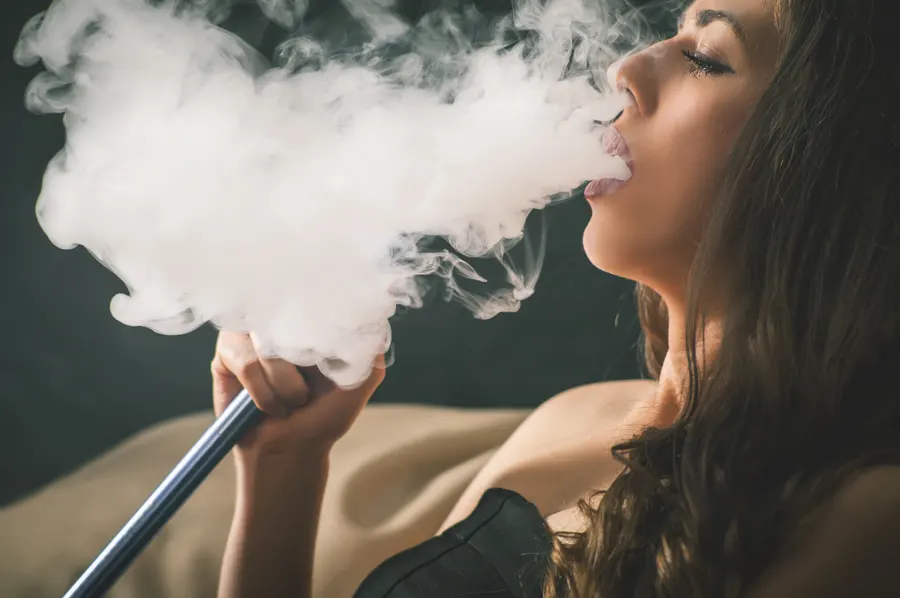 Detail: mladá žena vydychuje dym, fajčí vodnú fajku