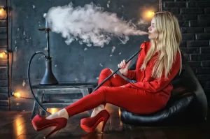 Mladá blind žena v červenom oblečení fajčí vodnú fajku a vydychuje dym