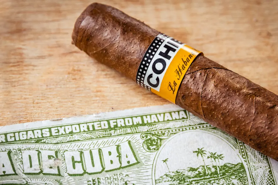 Cigara značky Cohiba položená na stole s bankovkou z Kuby