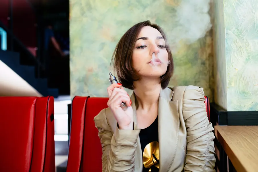 Mladá žena vydychuje paru z elektronickej cigarety