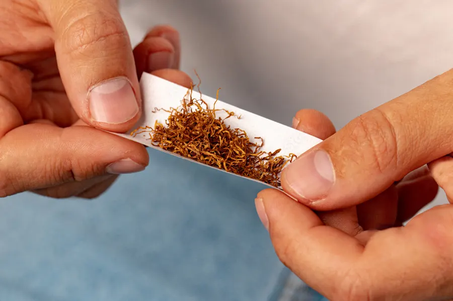Ručné balenie cigarety: cigaretový papierik s tabakom v mužských rukách