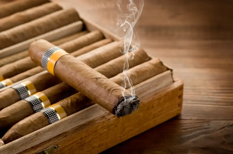 Zapálená cigara značky Cohiba položená na humidore s cigarami