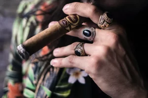 Detail ruky mladého muža s prsteňmi, ktorý fajčí cigaru s prstienkom